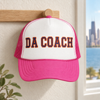 Da Coach embroidered foam trucker hat in white and pink on a wall hook