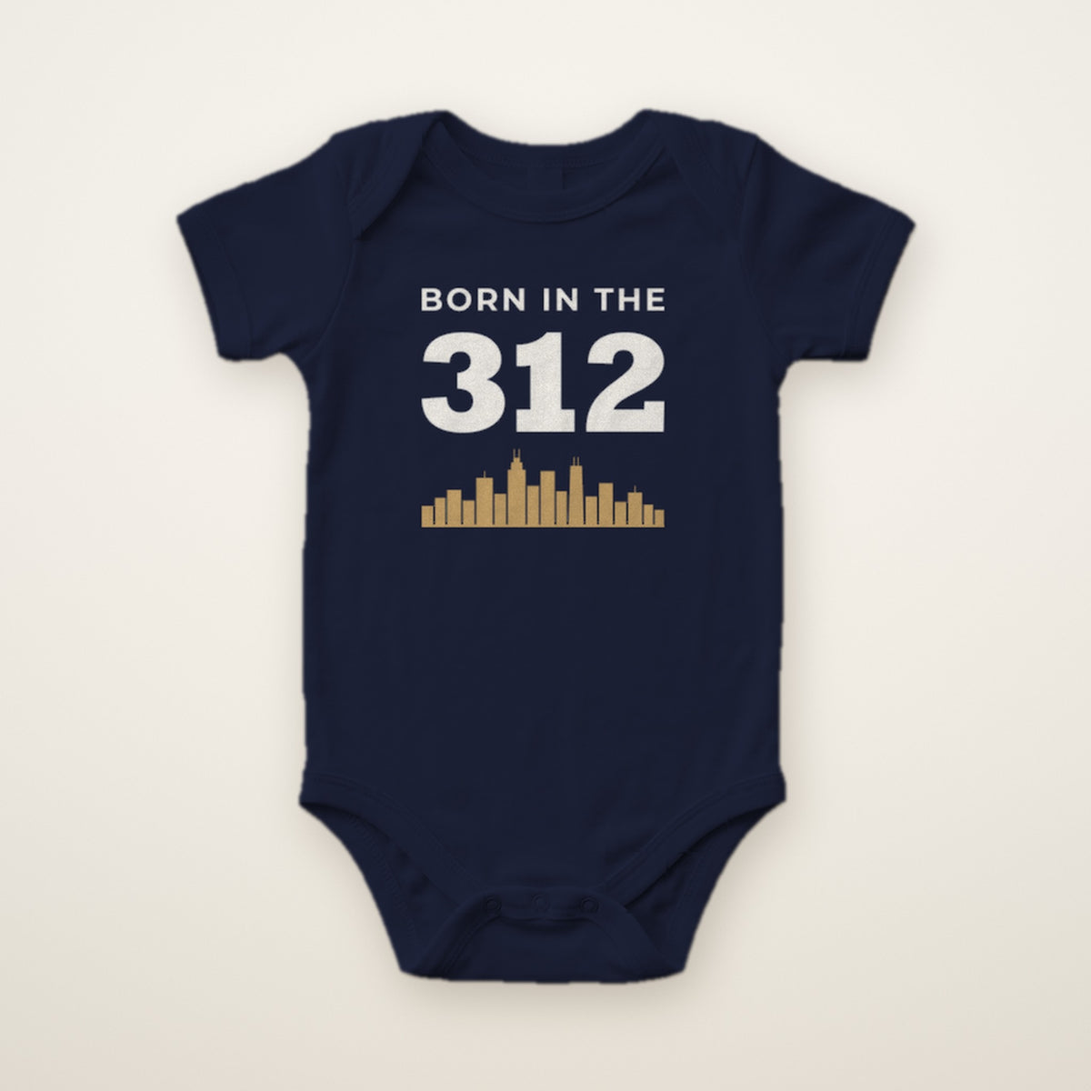 Born in the 312 baby bodysuit in Navy, flat lay with white 312 and gold Chicago skyline
