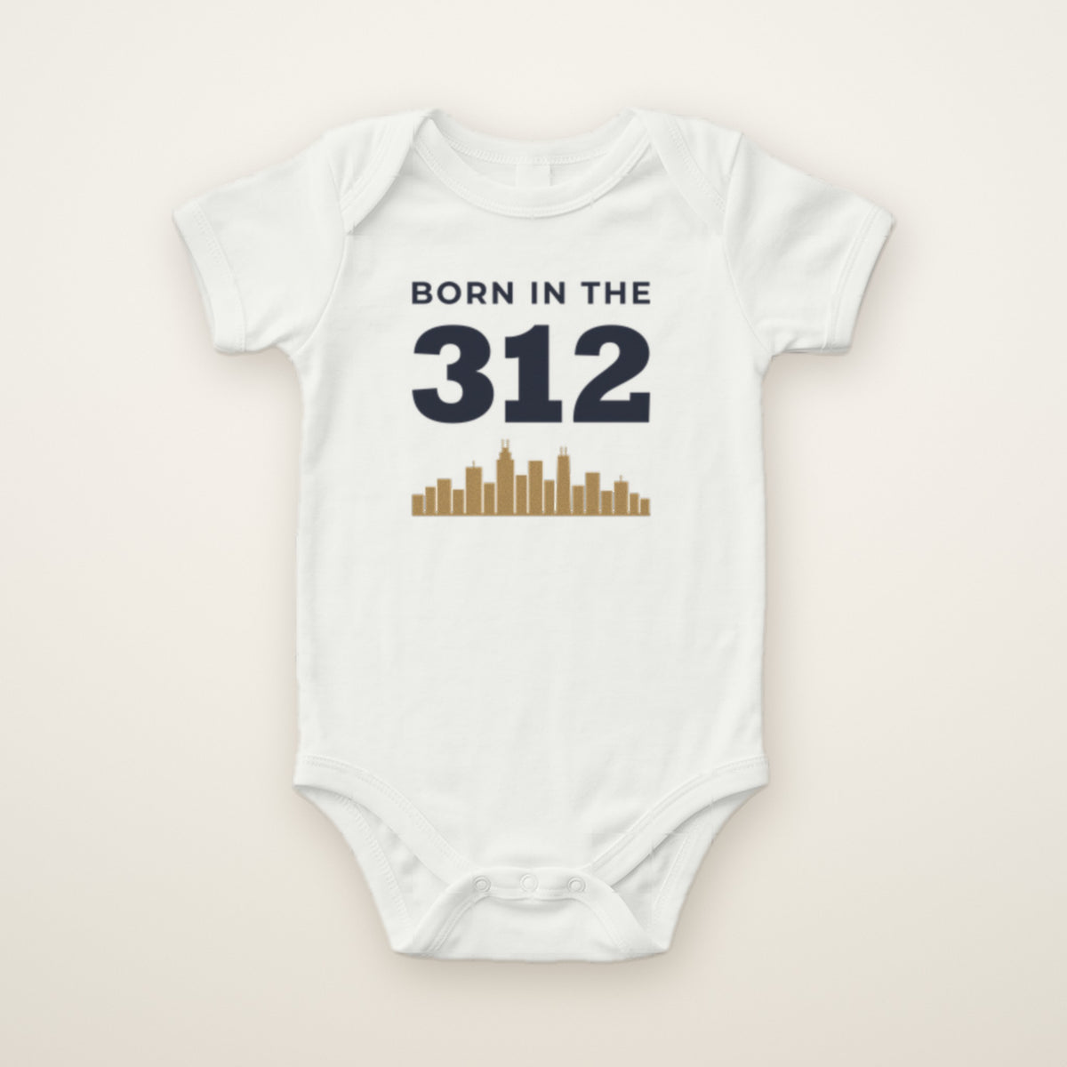 Born in the 312 baby bodysuit in White, flat lay with navy 312 and gold Chicago skyline