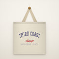 The Third Coast Canvas Tote Bag hanging from a brass peg on an ivory wall